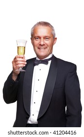 A Mature Male Wearing A Black Tuxedo And Bow Tie Raising A Glass Of Champagne, Isolated On A White Background.