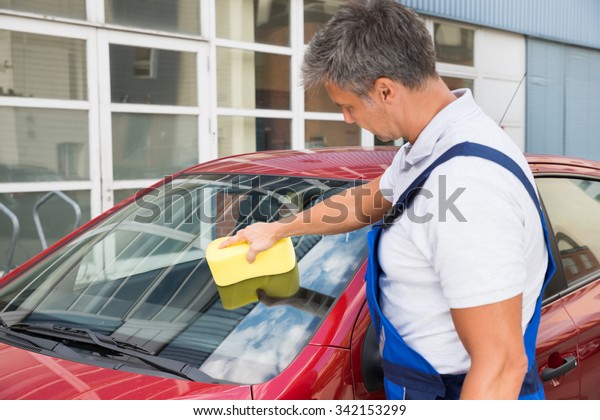 Mature\
male worker cleaning car windshield with\
sponge