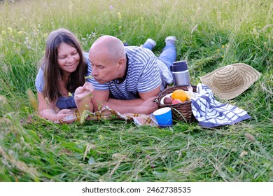 mature man 60 years old, woman 50 years old in blue clothes lie on grass in meadow, next to picnic basket with fruit, thermos with tea, concept of family picnic on nature, enjoy life, human happiness - Powered by Shutterstock