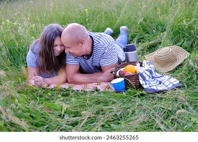 mature man 60 years old, woman 50 years old in blue clothes lie on grass in meadow, next to picnic basket with fruit, thermos with tea, concept of family picnic on nature, enjoy life, human happiness - Powered by Shutterstock