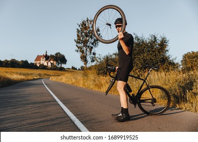 Mature Man In Active Wear, Protective Helmet And Mirrored Glasses Standing On Paved Road With Broken Bike. Bearded Bicyclist Holding Wheel In Hand And Trying To Fix His Vehicle.