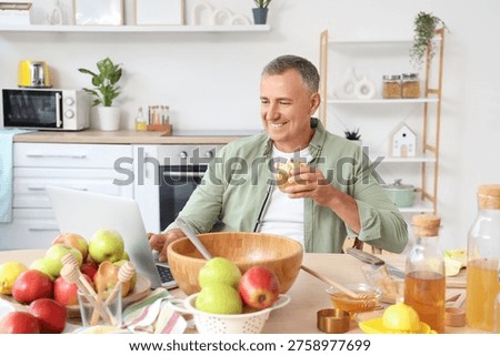 Mature man with apple cider using laptop at table in kitchen