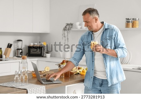 Mature man with apple cider using laptop in kitchen