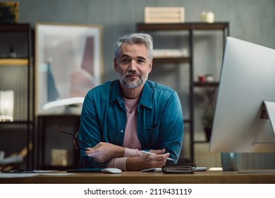 Mature man architect working on tablet at desk indoors in office, looking at camera.