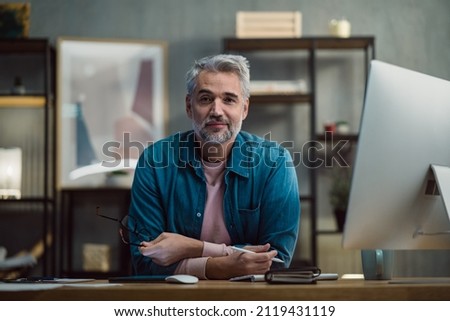 Mature man architect working on tablet at desk indoors in office, looking at camera.