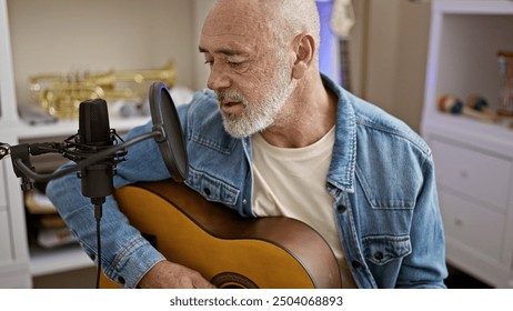 A mature man with a beard playing guitar and singing into a microphone in a home studio setting. - Powered by Shutterstock