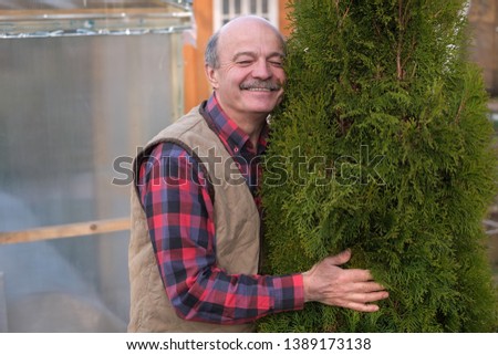 Mature man being proud of his garden. He embraces a tree trunk of green thuja. Stock photo © 