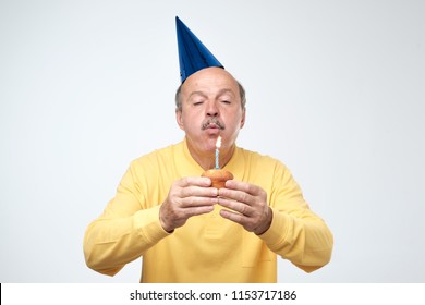 Mature man in birthday cap blowing candle on his cake making a wish. Happy birthday concept - Powered by Shutterstock