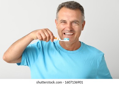 Mature Man Brushing Teeth On Light Background