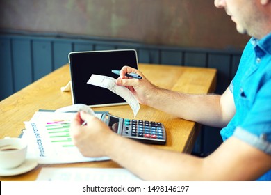 Mature Man Calculating Bills And Expenses Of Small Business - Man Holding Bills Paying Taxes With Internet Banking - Caucasian Male Working With Invoice On Table