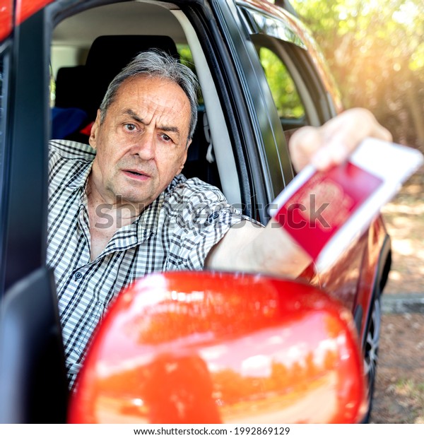 Mature man in a car showing his passport and\
Covid-19 vaccine record card. Traveling with vaccine passport of\
COVID-19. Caucasian man holding vaccine passport, sitting in the\
driver\'s seat of his\
car.