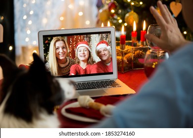 Mature man celebrating Christmas with his dog sitting at served holiday  table with laptop. People greeting their friends on video call using webcam. Christmas eve online. New normal social distancing - Powered by Shutterstock