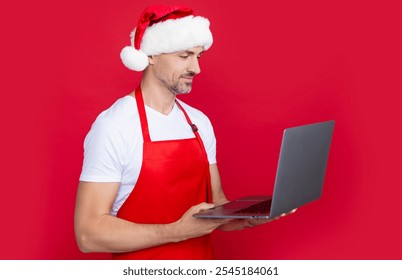 mature man in christmas santa hat and red apron hold computer - Powered by Shutterstock