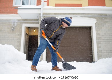 A mature man clean path near house from snow during strong blizzard. Person shoveling snow out of the driveway. Huge snowdrifts. Difficult situation in the city after a snow storm - Powered by Shutterstock