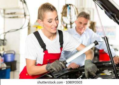 Mature Man - Client - And Young Female Car Mechanic Looking Under Auto Hood