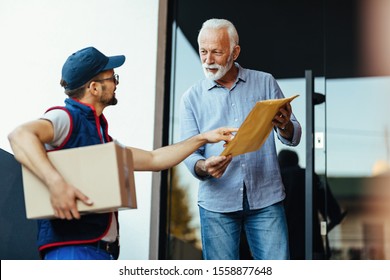 Mature Man Communicating With A Deliverer While Standing At Front Door And Receiving A Package. 