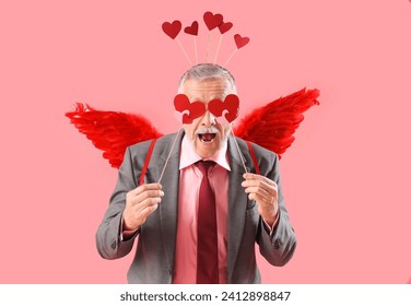 Mature man dressed as Cupid with hearts on pink background. Valentine's Day celebration