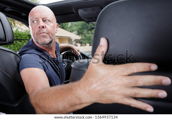 mature man driving a car in\
reverse