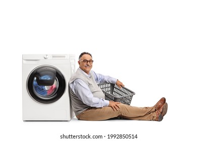 Mature Man With An Empty Laundry Basket Sitting And Leaning On A Washing Machine Isolated On White Background