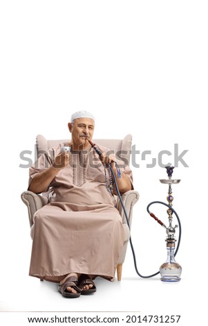 Mature man in ethnic clothes sitting in an armchair and smoking shisha isolated on white background