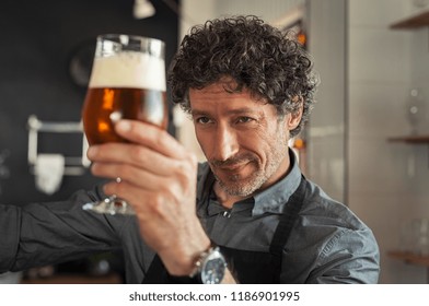 Mature man examining the quality of craft beer at brewery. Inspector working at alcohol manufacturing factory checking beer. Man in distillery checking quality control of draught beer. - Powered by Shutterstock