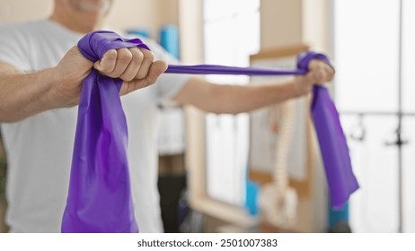 Mature man exercising with resistance band in a bright physiotherapy clinic - Powered by Shutterstock