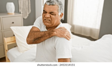 Mature man experiencing shoulder pain in a bedroom setting, conveying issues of health and aging. - Powered by Shutterstock