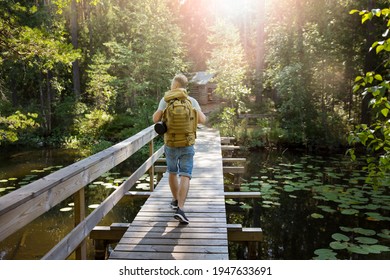 Reifender Mann, der im Sommer die finnische Natur erforscht und die Brücke überquert. Wanderer mit großem Rucksack, der in Wäldern reist. Sommerskandinavische Seen- und Waldlandschaft. 