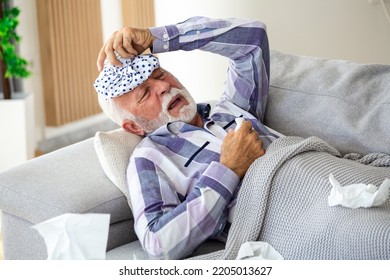 Mature Man Feeling Sick With Cold And Fever At Home, Ill With Flu Disease Sitting On The Sofa With Ice Pack On His Head