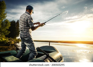 Mature man fishing from the boat on the pond at sunset