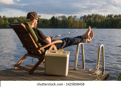 Mature Man Fishing From Wooden Pier Near Cottage On Lake In Finland At Summer