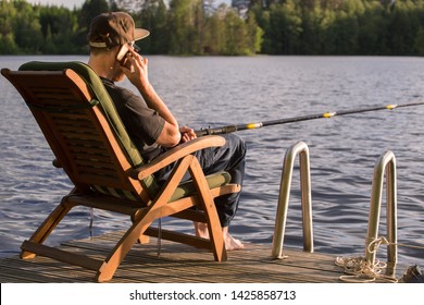 Mature Man Fishing From Wooden Pier Near Cottage On Lake In Finland At Summer