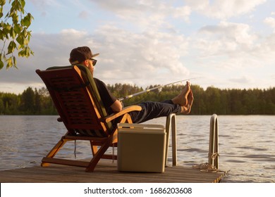 Mature man fishing from wooden pier near cottage on lake in Finland at summer