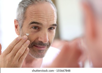 Mature man in front of mirror applying cosmetics