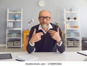 Mature man with a gray beard looks at the camera, speaks with his partner sitting at a table in the office at home. - Powered by Shutterstock