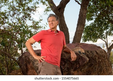 Mature Man Hanging Out At The Park Wearing Casual Clothes And Leaning Against A Big Rock