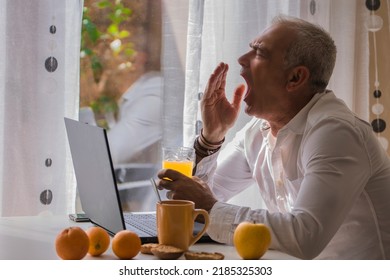 mature man having breakfast and stretching in front of the computer