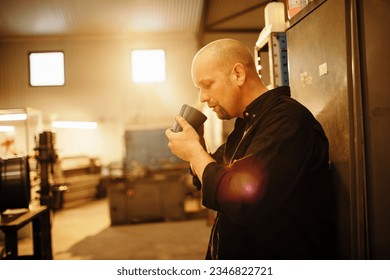 Mature man having a coffee break while working in a workshop - Powered by Shutterstock