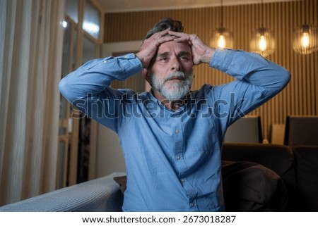Mature man having panic attack at home, holding head in distress, experiencing anxiety disorder symptoms and triggers, mental health concern and stress