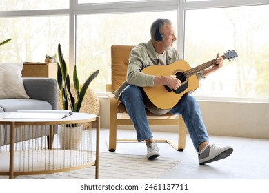 Mature man in headphones playing guitar at home - Powered by Shutterstock