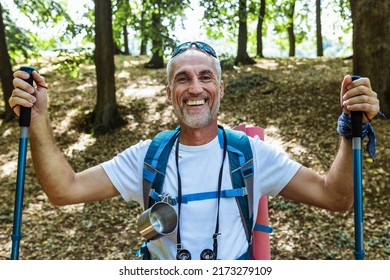 Mature Man Hiking In The Wood. Handsome Middle Aged Caucasian Man With Backpack And Hiking Poles.