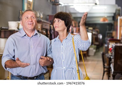 Mature Man With His Wife Are Choosing Furniture At Antique Shop. Focus On Both Persons