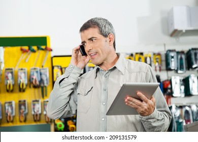 Mature man holding digital tablet while using mobilephone in hardware store - Powered by Shutterstock