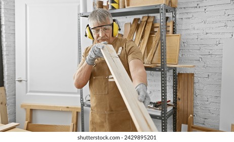 A mature man inspects wood in his carpentry workshop while wearing protective gear. - Powered by Shutterstock