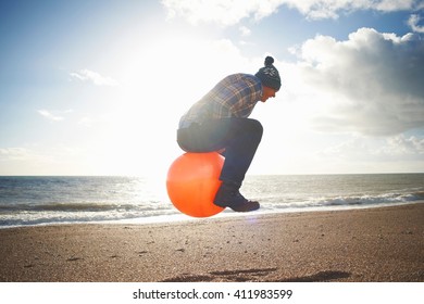 Mature Man Jumping Mid Air On Inflatable Hopper At Beach