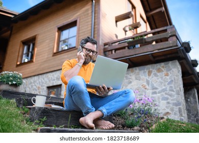Mature man with laptop and smartphone working outdoors in garden, home office concept. - Shutterstock ID 1823718689