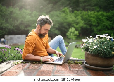 Mature man with laptop working outdoors in garden, home office concept.