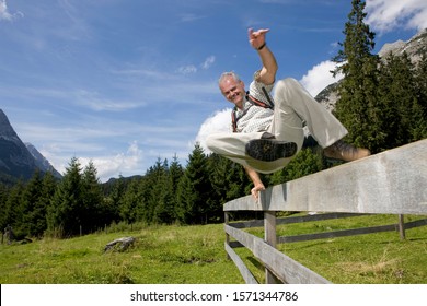 Mature man leaping over fence in countryside