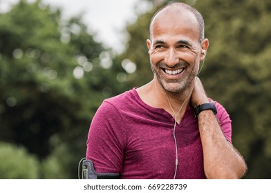 Mature man listening to music while resting after jogging. Happy senior man feeling refreshed after exercise. Portrait of a multiethnic man looking away in park while listening to music after fitness. - Powered by Shutterstock