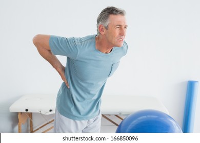 Mature Man With Lower Back Pain Standing In The Gym At Hospital